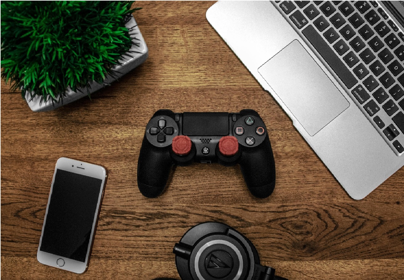 A table with a plant, computer, and video game controller on it